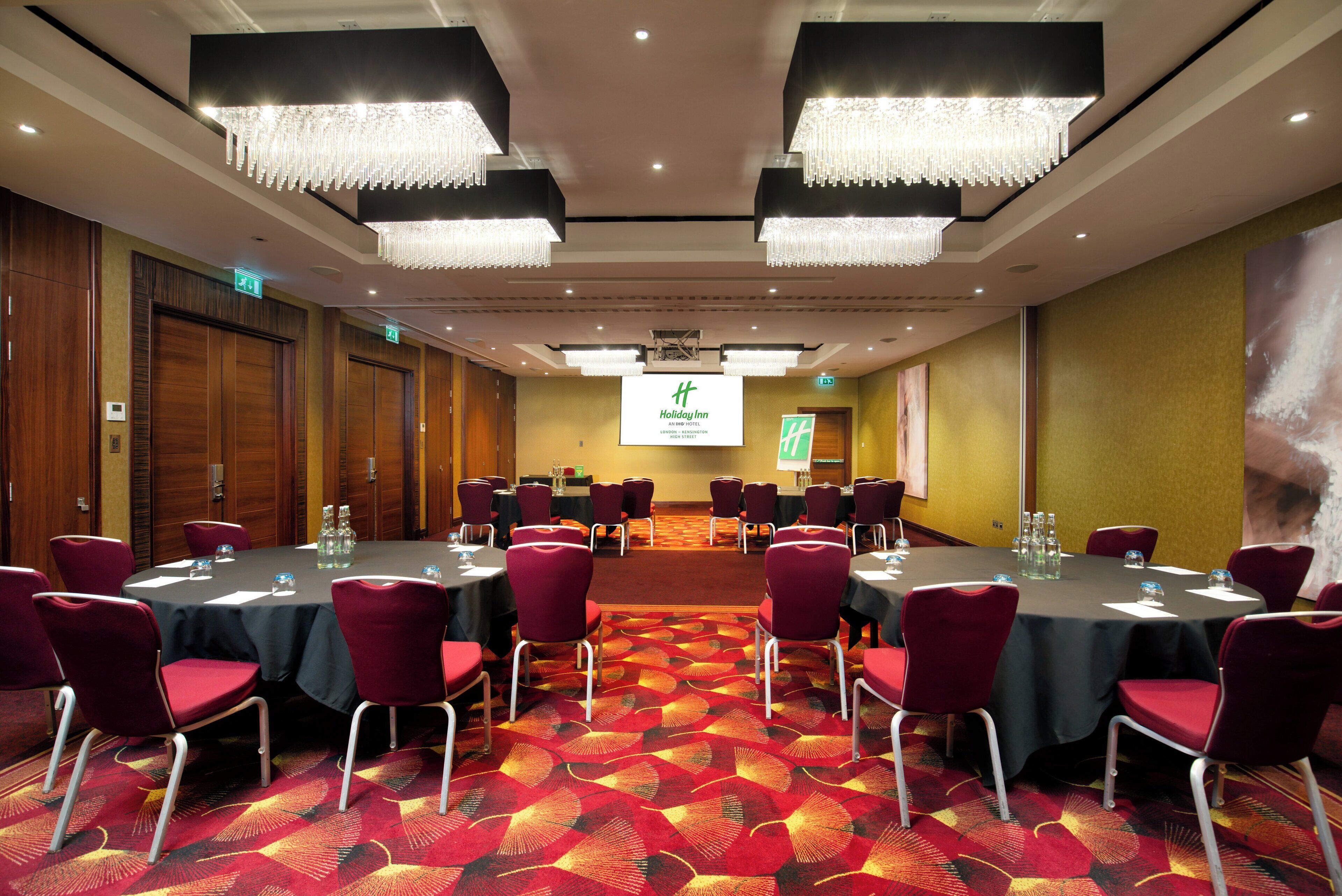 A conference room with round tables, red chairs, and a carpeted floor.