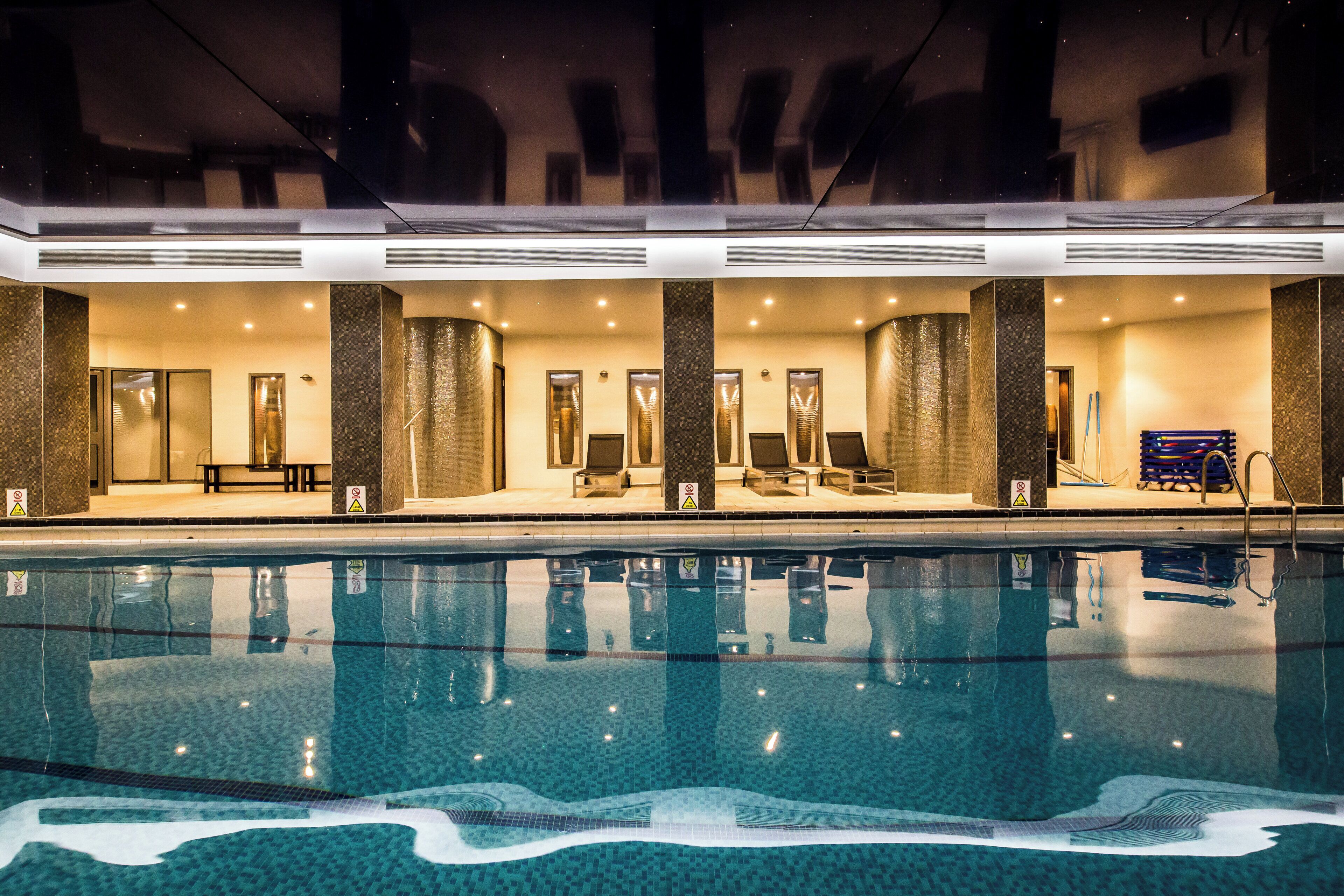 Zona de piscina de hotel con piscina cristalina, sillas de descanso y un área de estar cubierta.