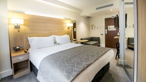A hotel room with a large bed, bedside tables, a desk, a chair, and a small sofa.