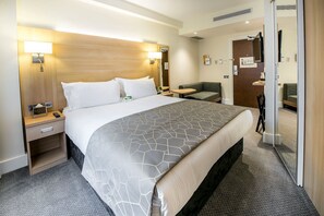 Una camera d'albergo con un letto grande, comodini, una scrivania, una sedia e un piccolo divano.