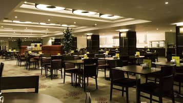 A modern dining area with multiple tables and chairs, overhead lighting, and a central plant.