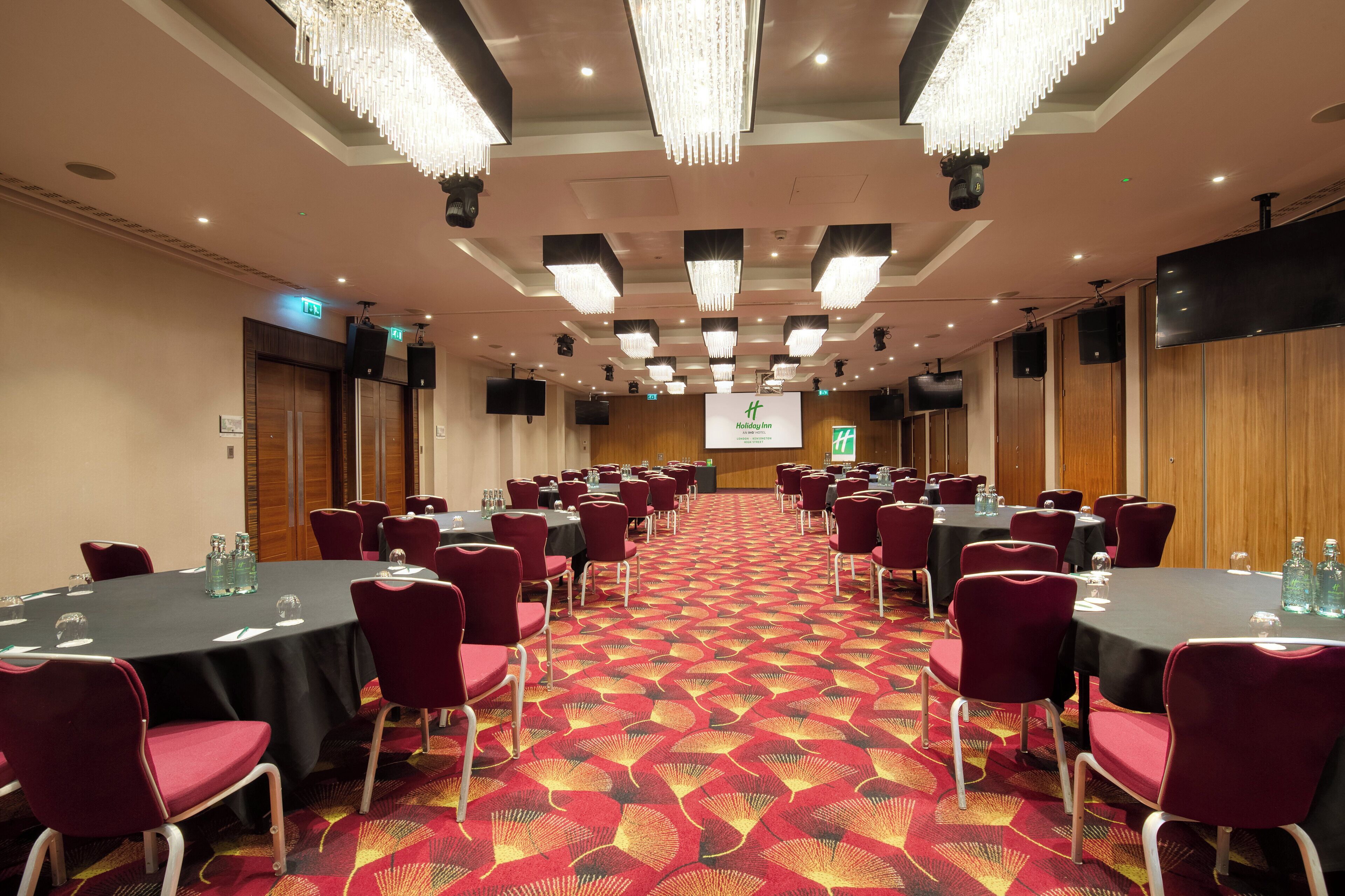 A conference room with round tables, red chairs, and a patterned carpet.