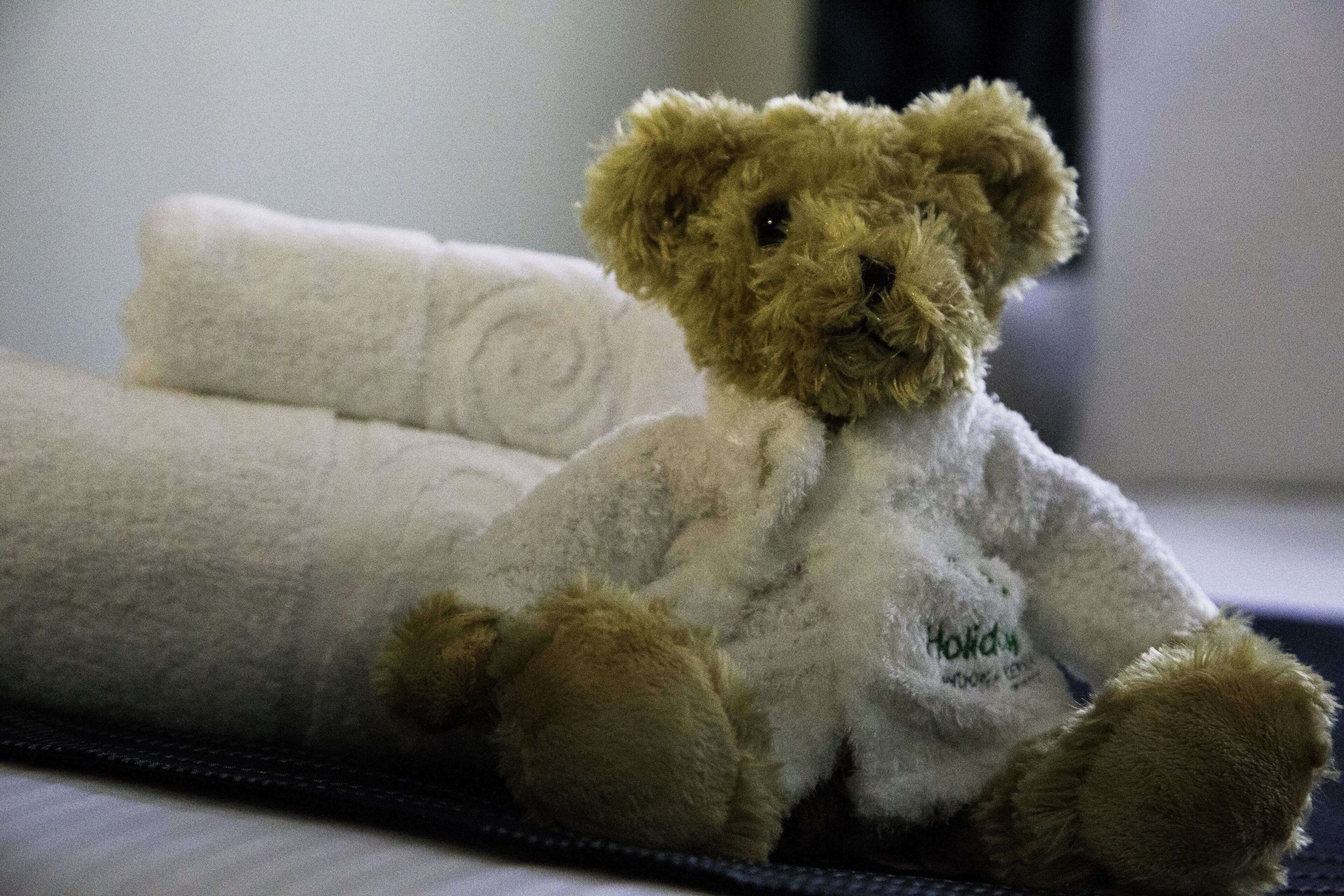 Un osito de peluche sentado sobre una cama con un almohadón blanco y una manta.