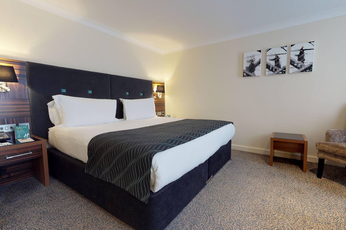Una camera d'albergo con un letto grande, comodini, una sedia e un'opera d'arte appesa al muro.