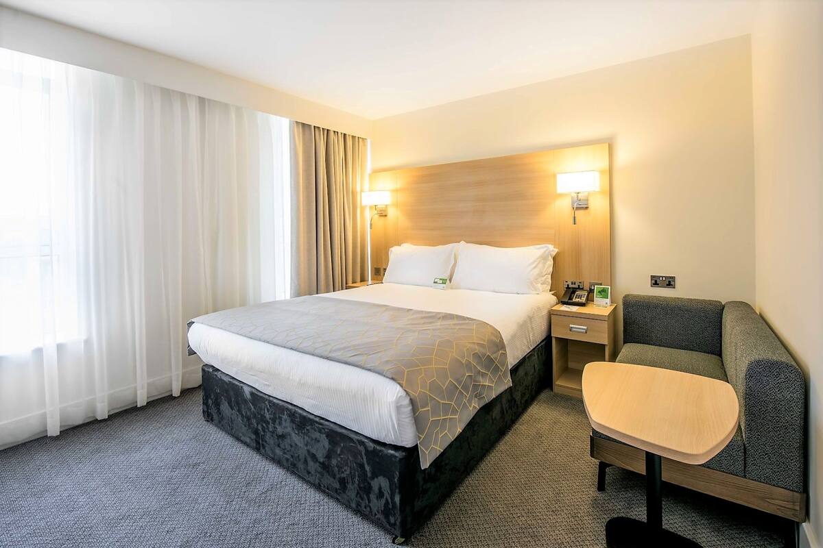 Una camera d'albergo con un letto, un comodino, una lampada e un piccolo angolo salotto.
