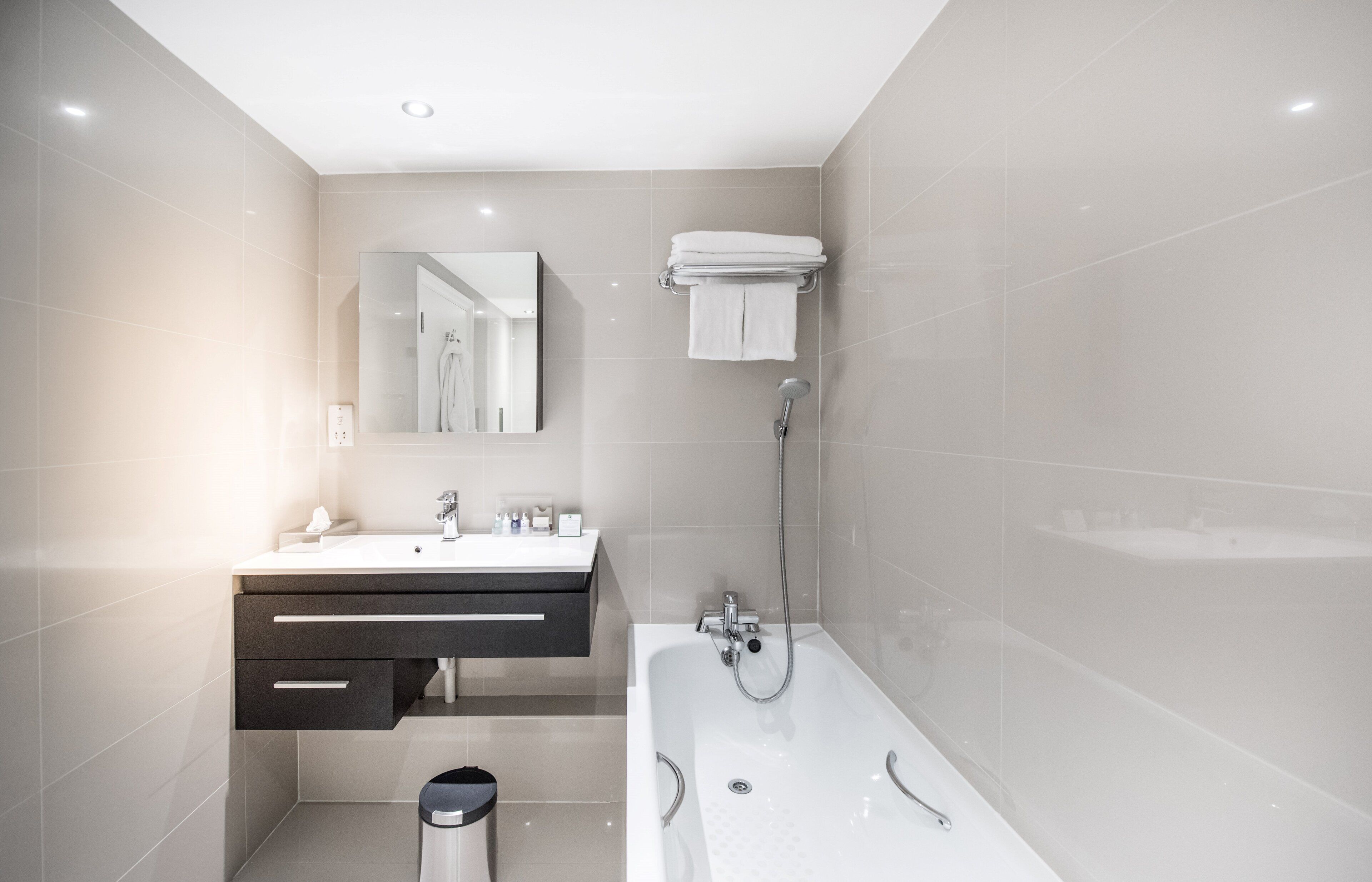 Un bagno moderno con un lavandino bianco, un mobile contenitore scuro, un ampio specchio, una vasca e un portascope.