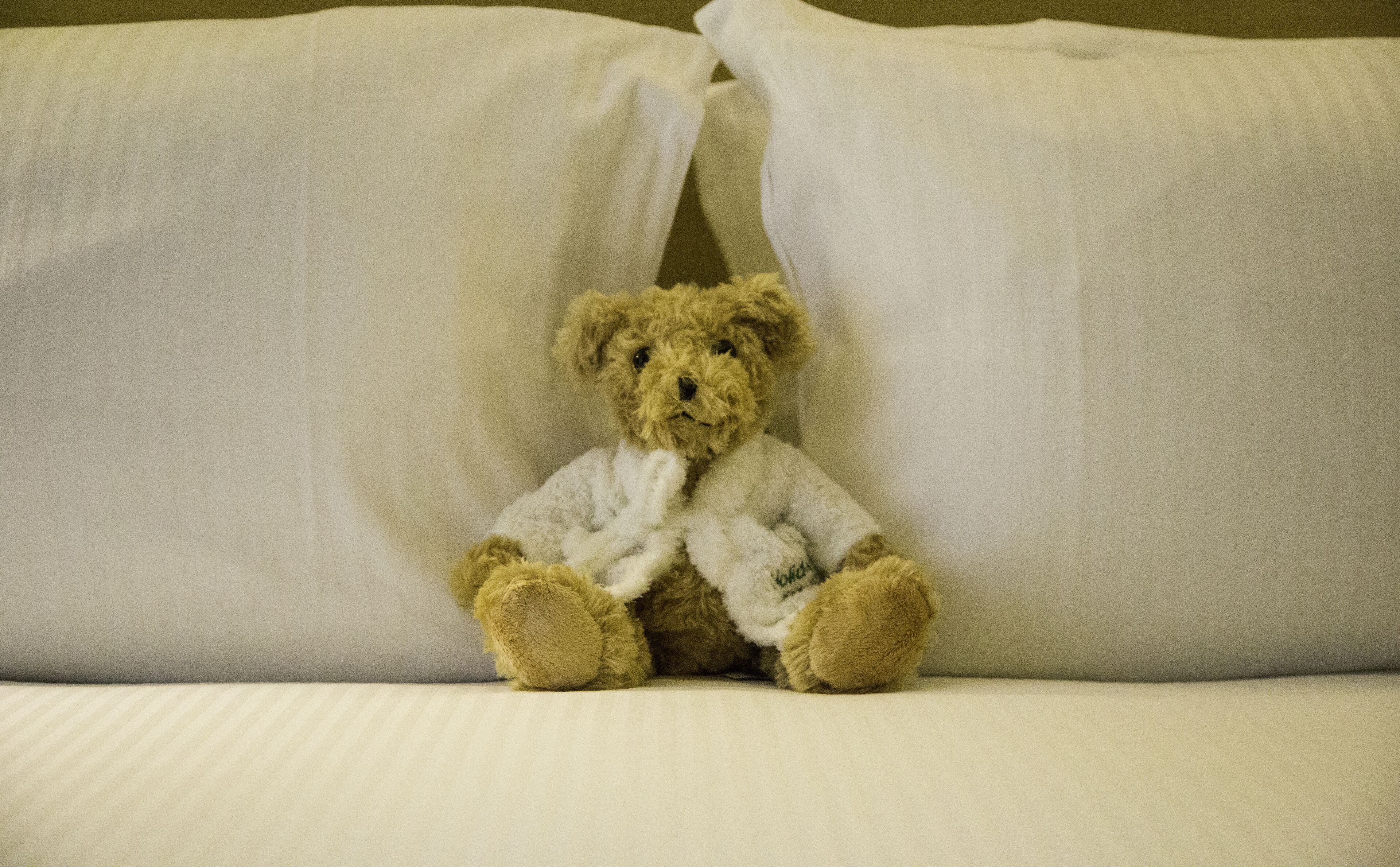 A teddy bear sitting on a bed with white sheets.
