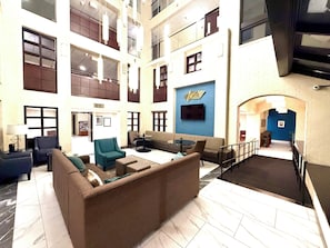 A spacious lobby with high ceilings, multiple seating areas, and a staircase leading to upper floors.
