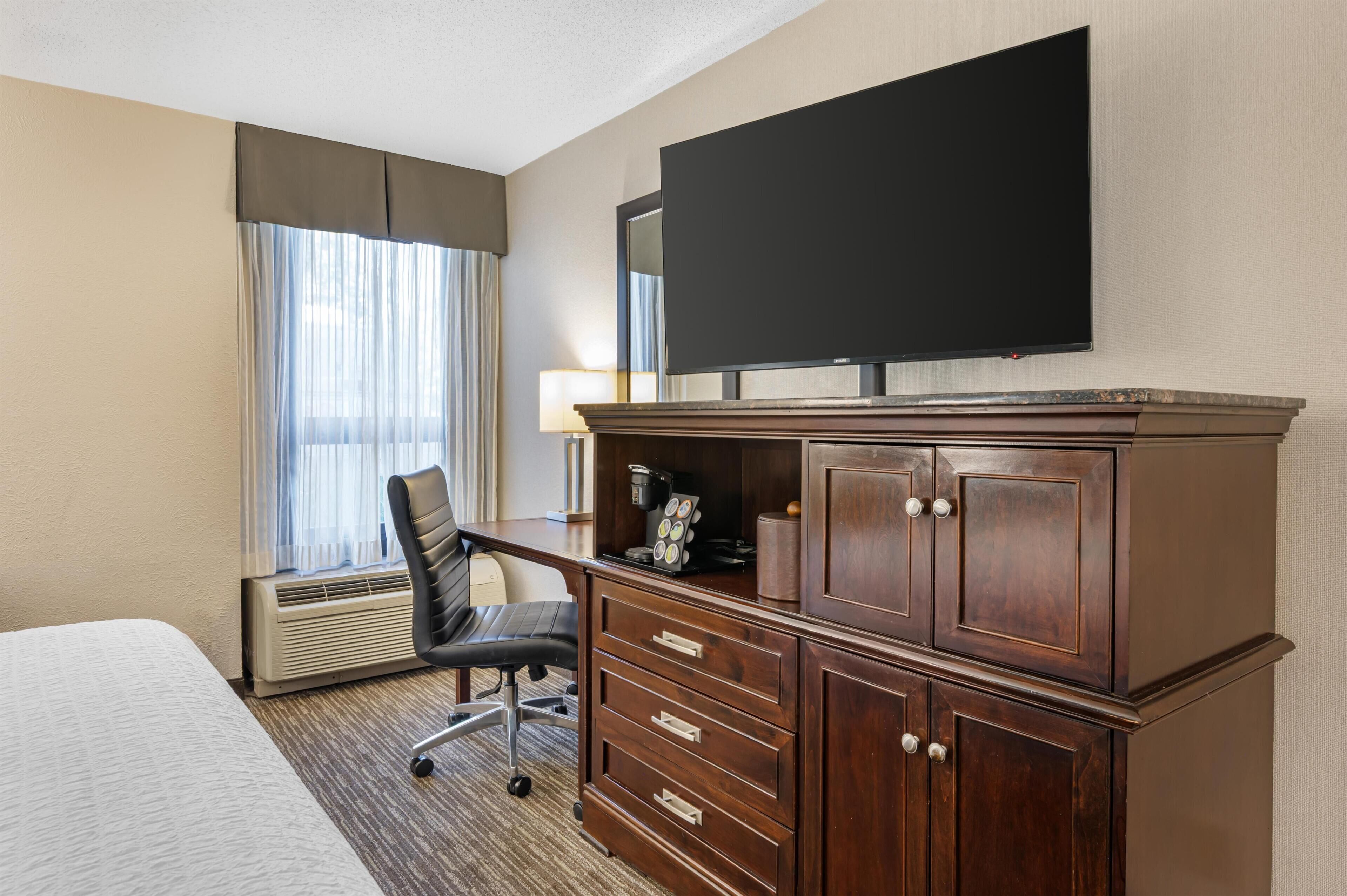 Habitación de hotel con cama, escritorio, silla, televisor y minibar.