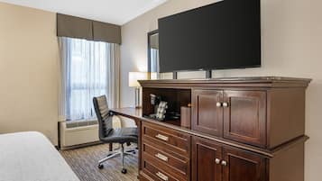 Habitación de hotel con cama, escritorio, silla, televisor y minibar.