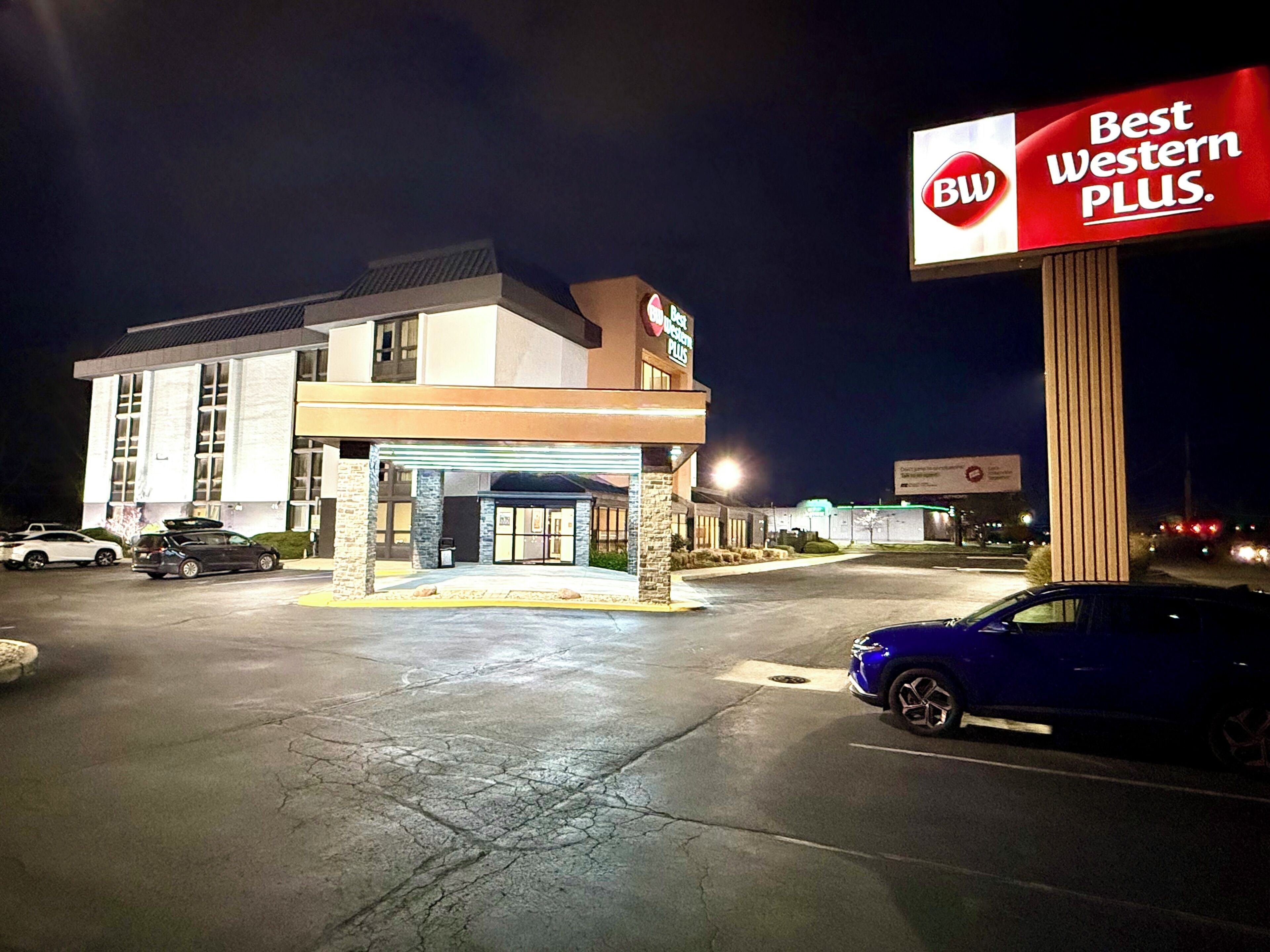 A Best Western Plus hotel with a modern facade, a covered entrance, and a parking lot at night.