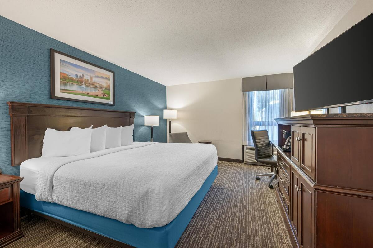 A hotel room with a large bed, a desk, a chair, a TV, and a painting on the wall.