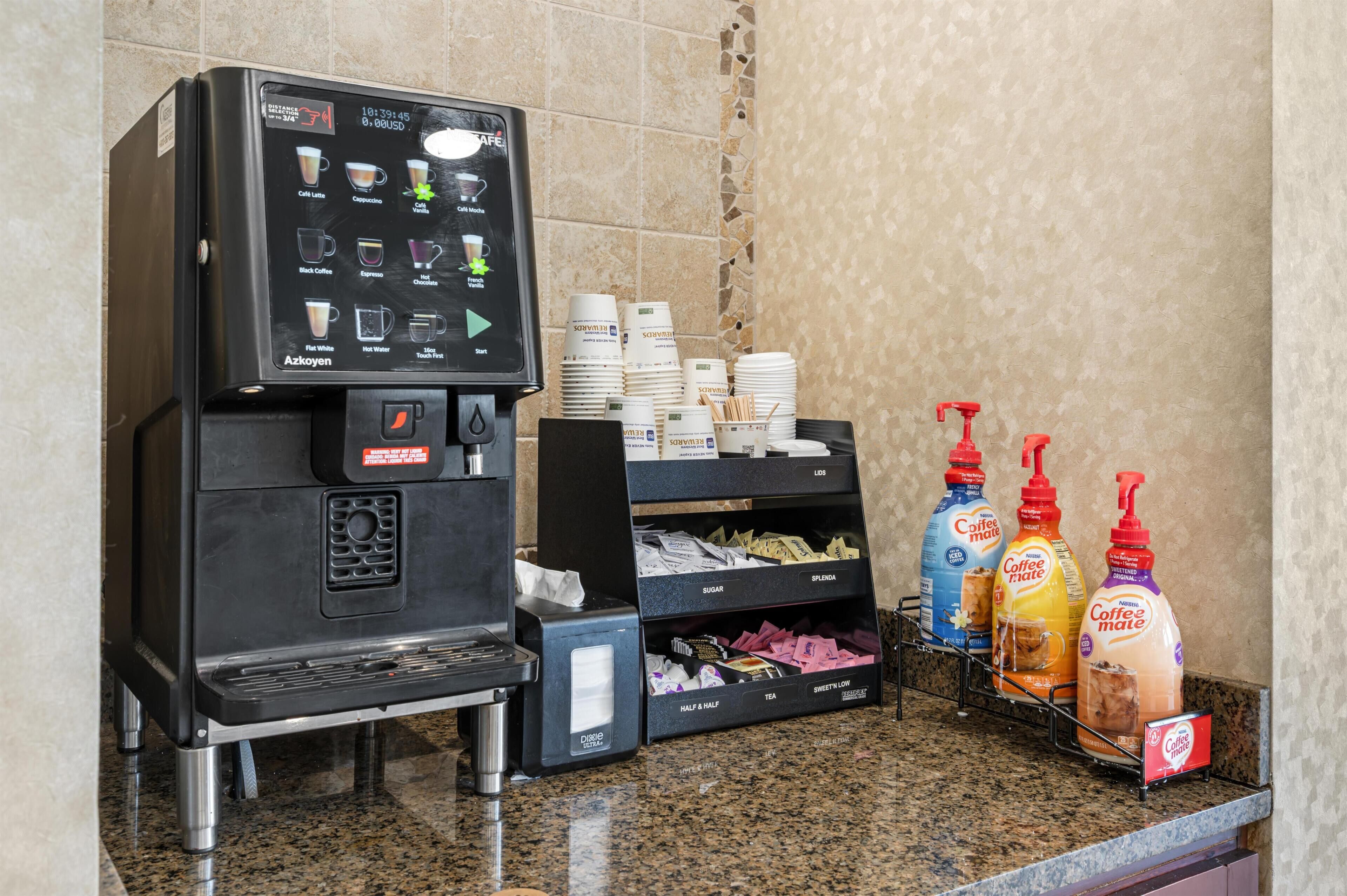 Een koffiehoek met een koffieapparaat, wegwerpbekers en koffiedranken.