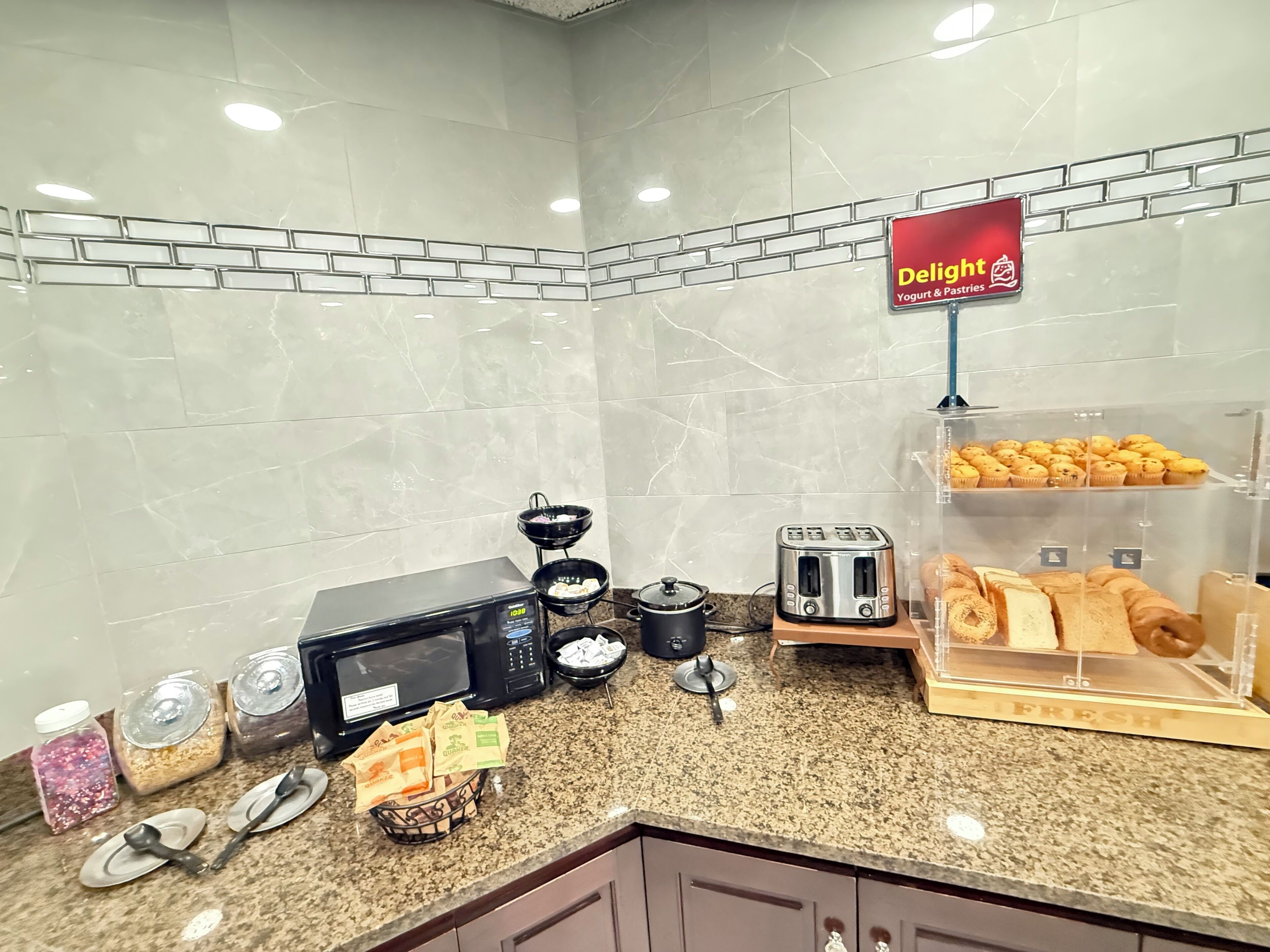 A kitchen area with a microwave, toaster, and a display of pastries.