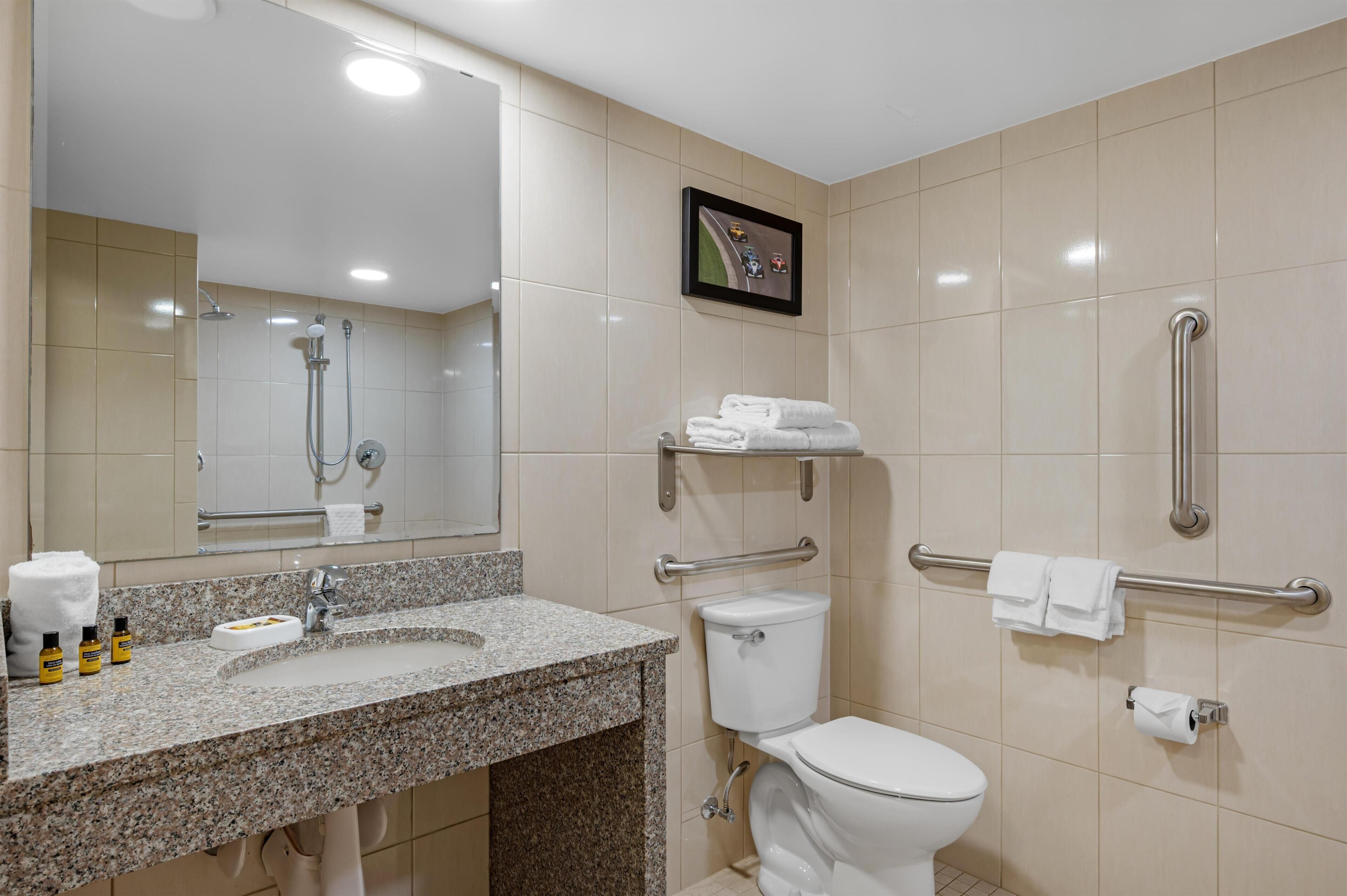 Un baño con lavamanos de granito, inodoro, ducha y barra de apoyo.