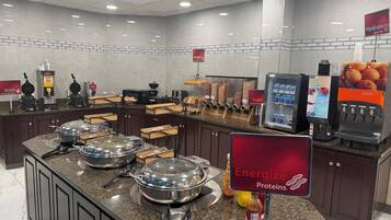 Montaje de bufé con distintas estaciones de comida, una barra de jugos y un letrero que promociona Proteínas Energizantes.