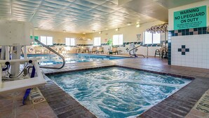 An indoor swimming pool with a lifeguard station, lounge chairs, and a warning sign about lifeguard duty.