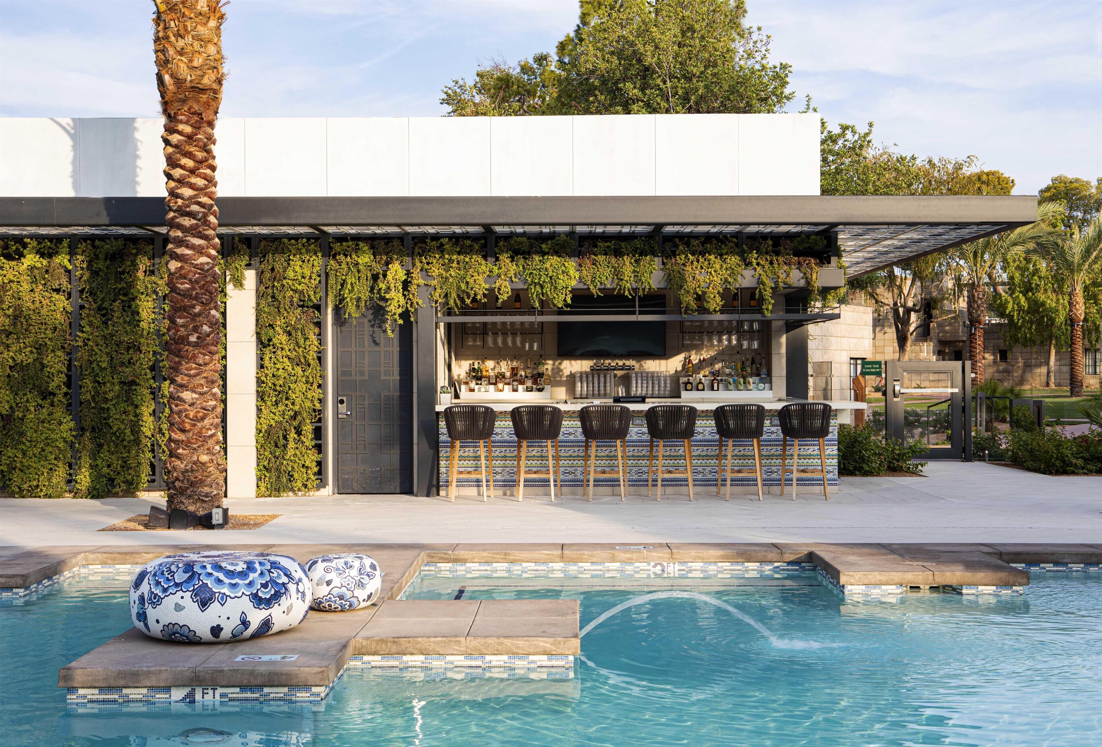 A modern outdoor bar area with a pool, seating, and a pergola with greenery.