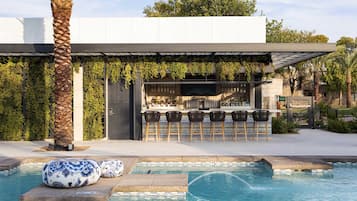 A modern outdoor bar area with a pool, seating, and a pergola with greenery.