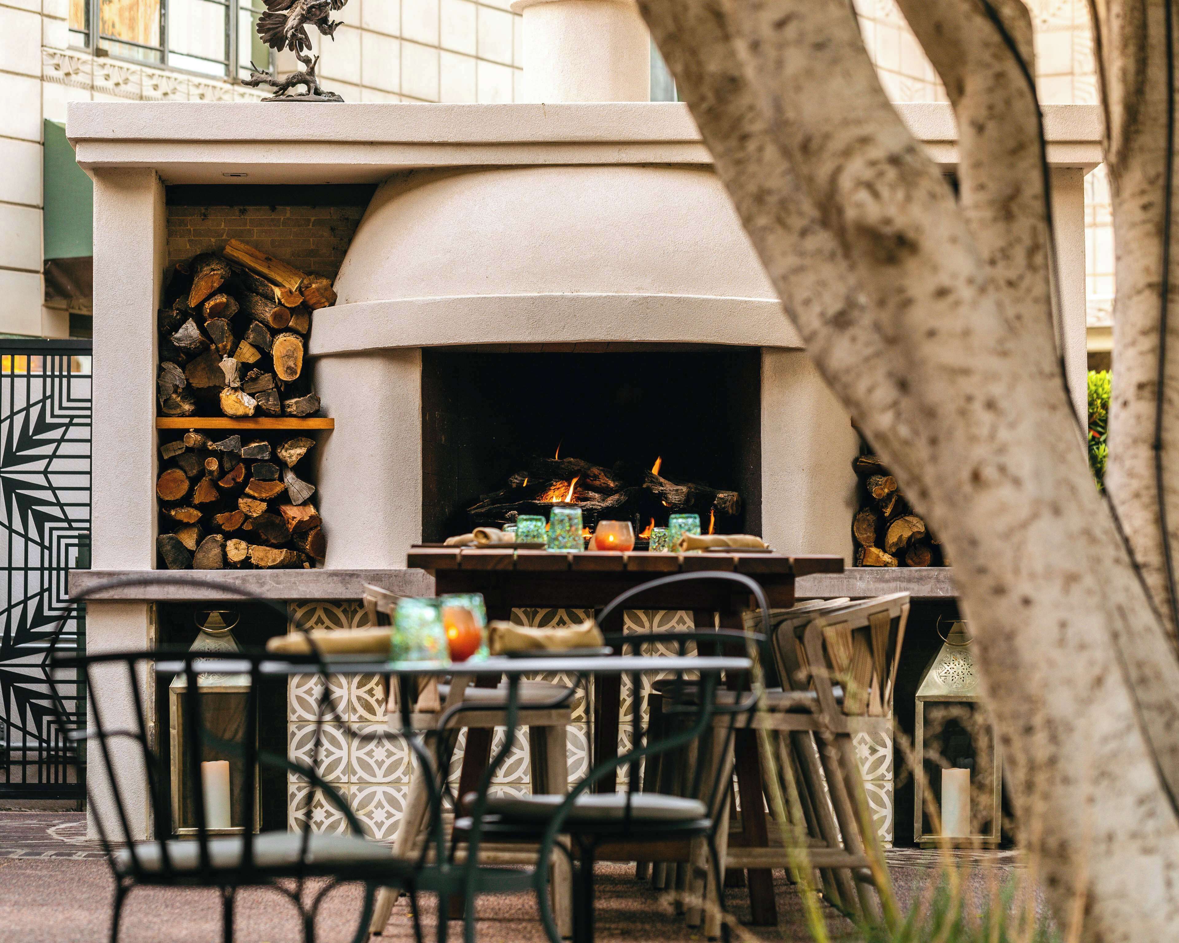 An outdoor seating area with a stone fireplace, wooden logs, and a lantern.