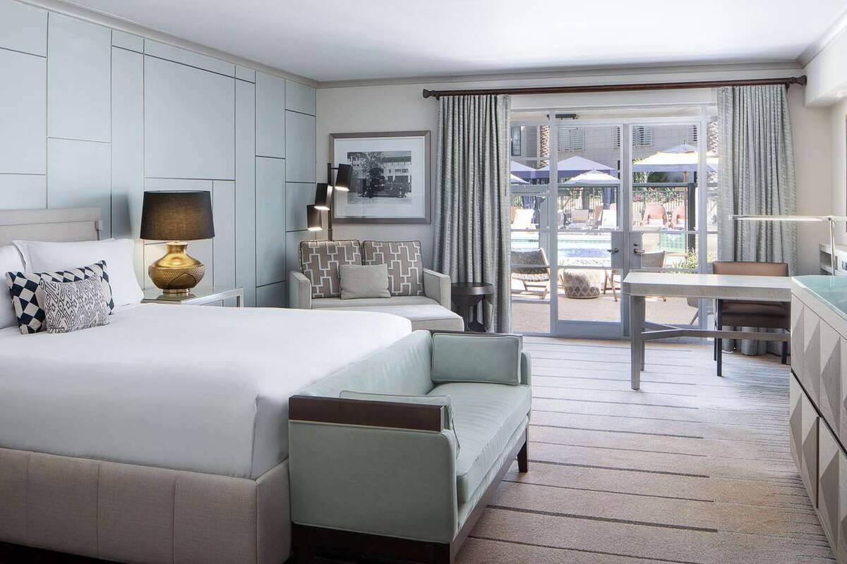 A hotel room with a large bed, a desk, and a view of the outdoor pool area.