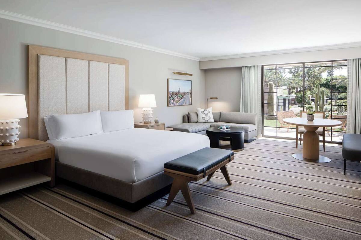 A hotel room with a large bed, a sofa, a small table, and a view of the outdoors.