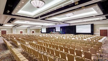 A large conference room with rows of chairs, a stage with a podium, and a large screen.