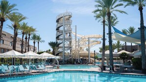 A pool area with lounge chairs, a water slide, and palm trees.