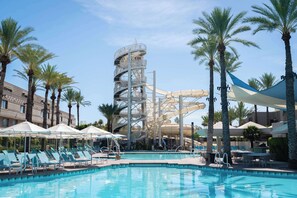 A pool area with lounge chairs, a water slide, and palm trees.