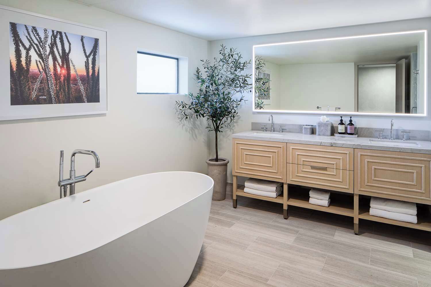 A modern bathroom with a freestanding bathtub, a large mirror, and a potted plant.