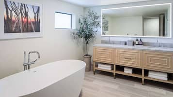 A modern bathroom with a freestanding bathtub, a large mirror, and a potted plant.