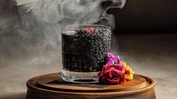A glass with a dark liquid and a flower on a wooden coaster.