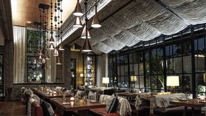 A spacious dining area with multiple tables and benches, large windows offering a view of the outdoors, and hanging pendant lights. - Arizona Biltmore, LXR Hotels & Resorts (Phoenix)