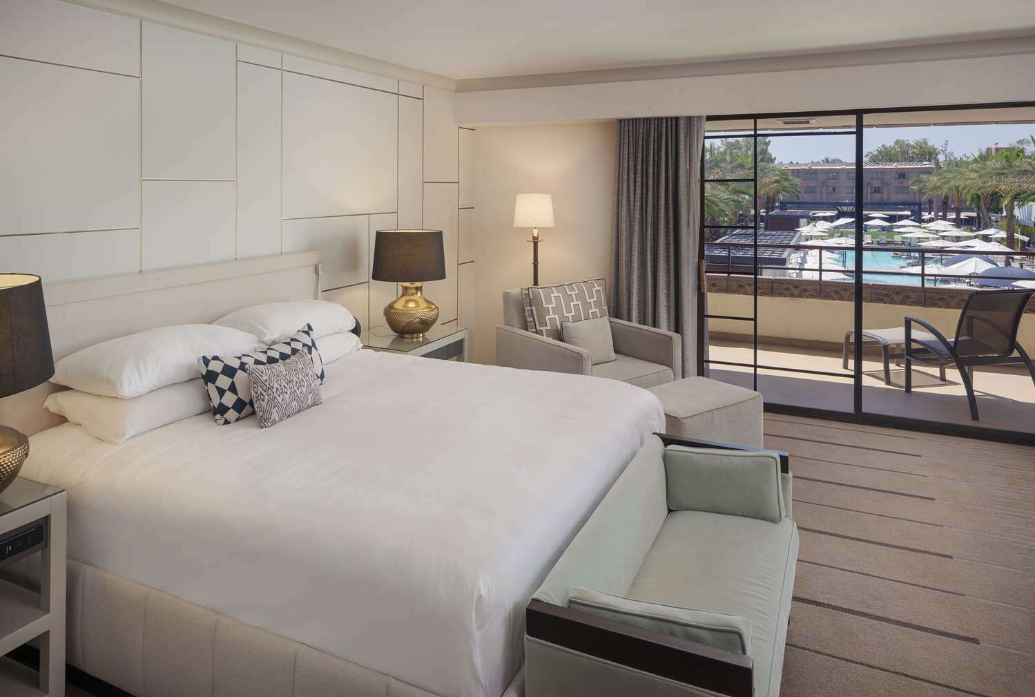 A hotel room with a large bed, a desk, a chair, and a view of a pool.