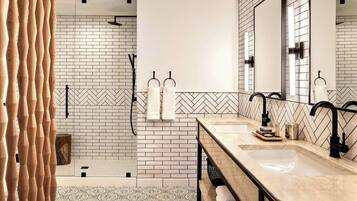 A modern bathroom with a large mirror, two sinks, and a shower area.