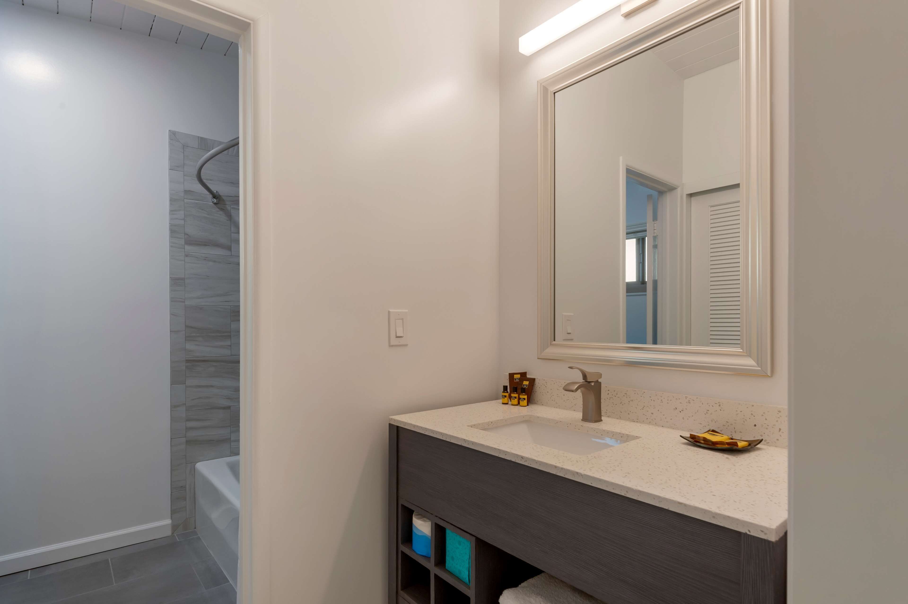 Un baño moderno con tocador blanco, un espejo grande y zona de ducha.
