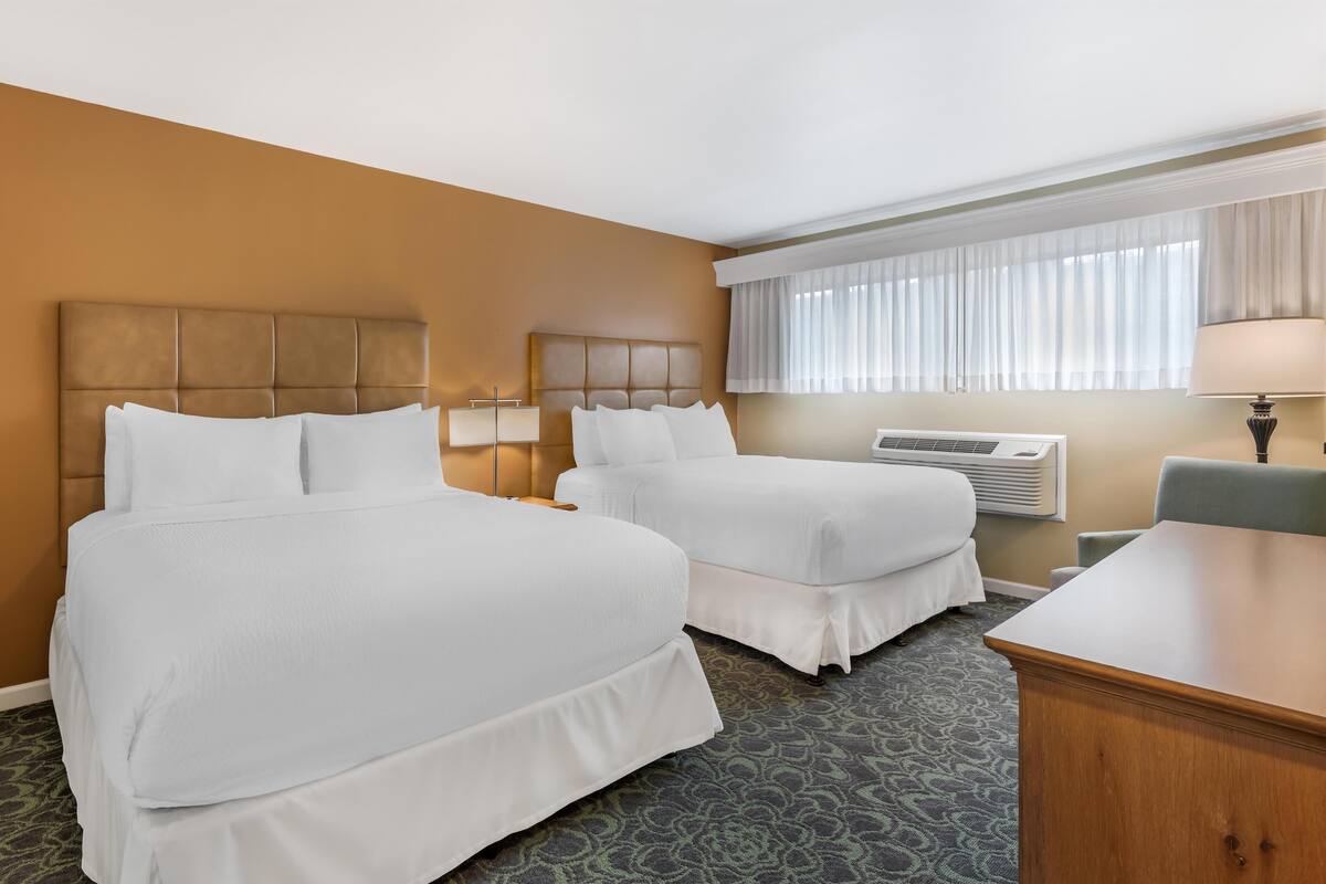 Une chambre d’hôtel avec deux lits, un bureau, une chaise, une lampe et un appareil de climatisation.