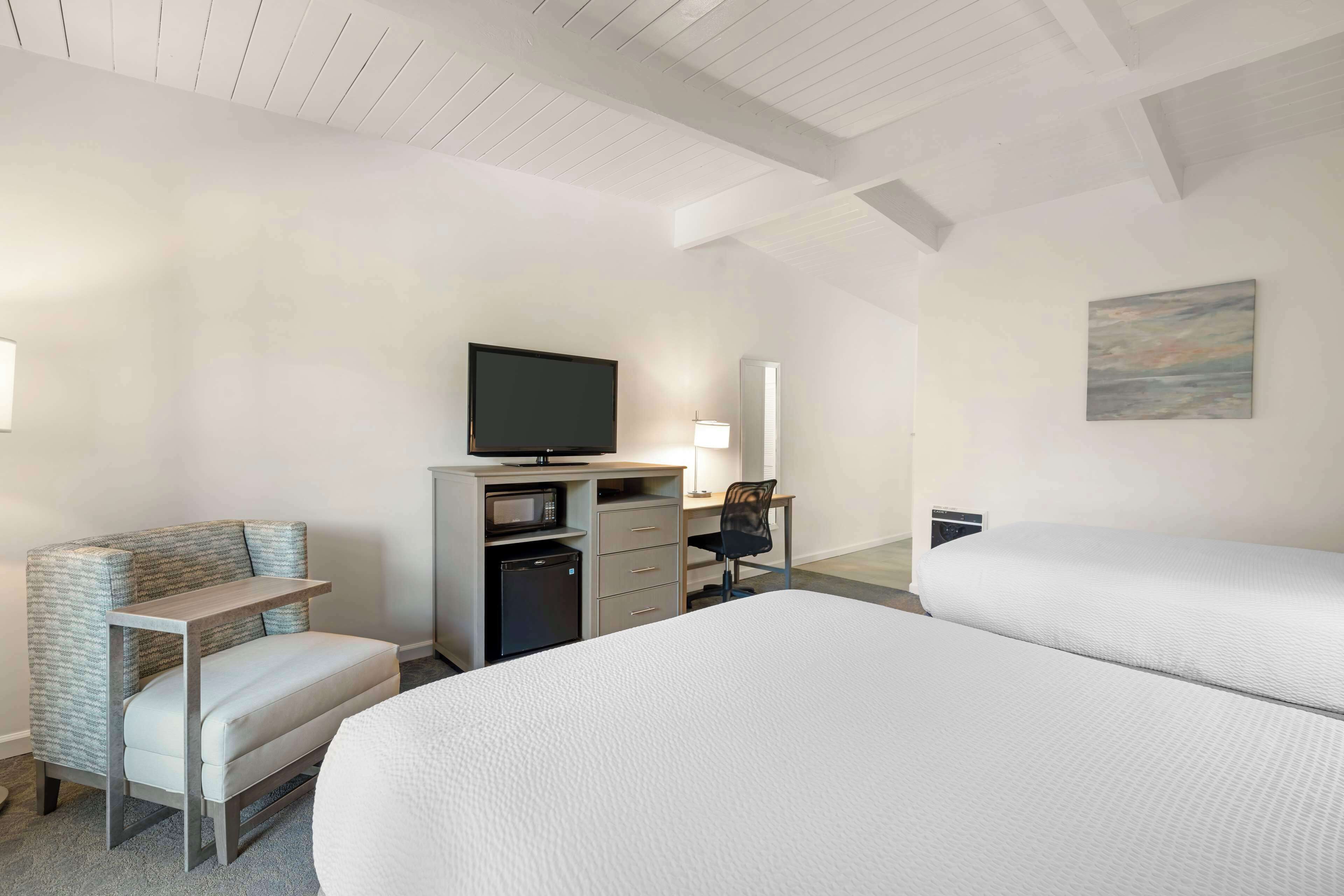 A hotel room with two beds, a desk with a computer, a television, and a microwave.