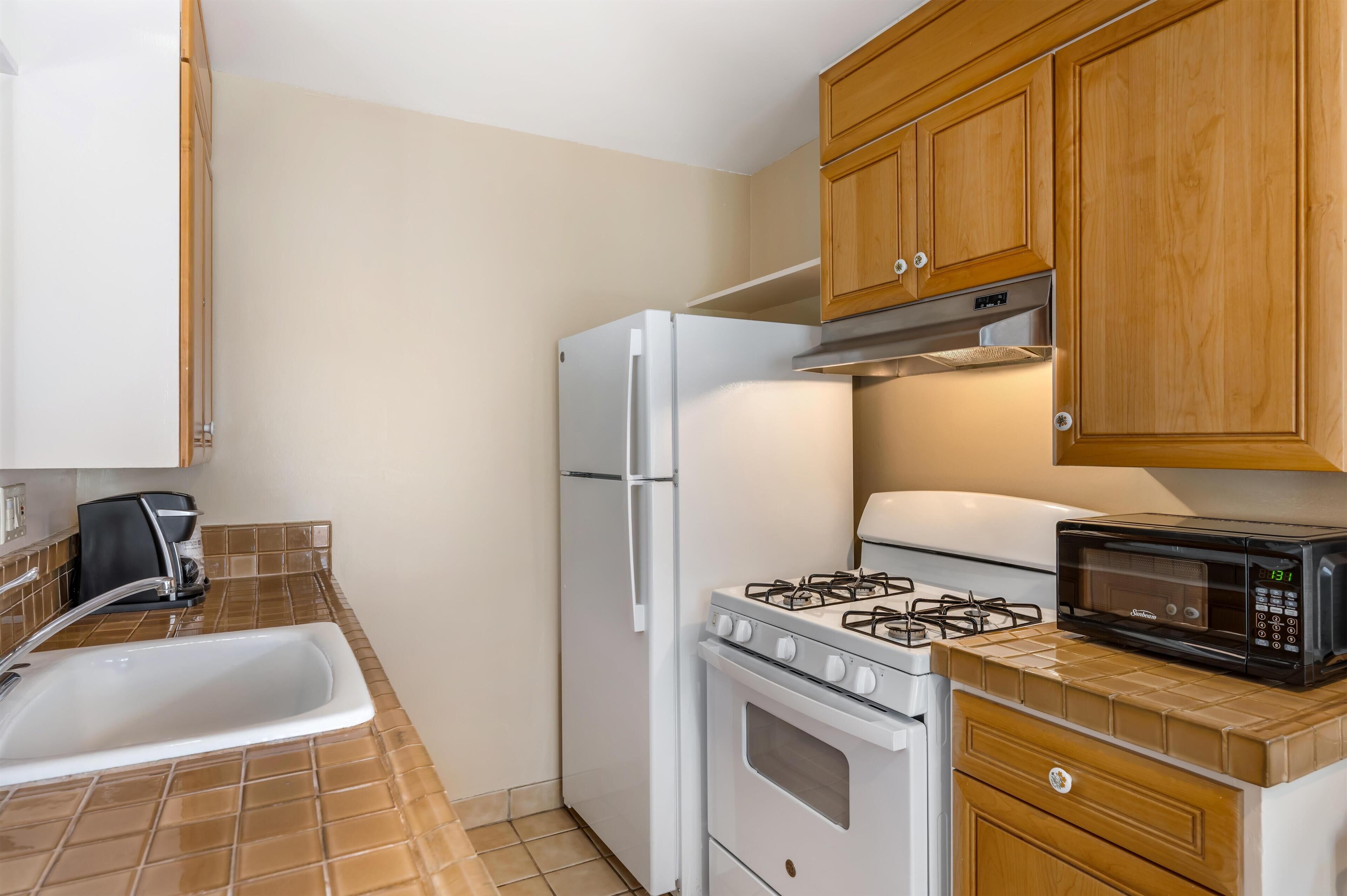 A compact kitchen with a white refrigerator, stove, and microwave.