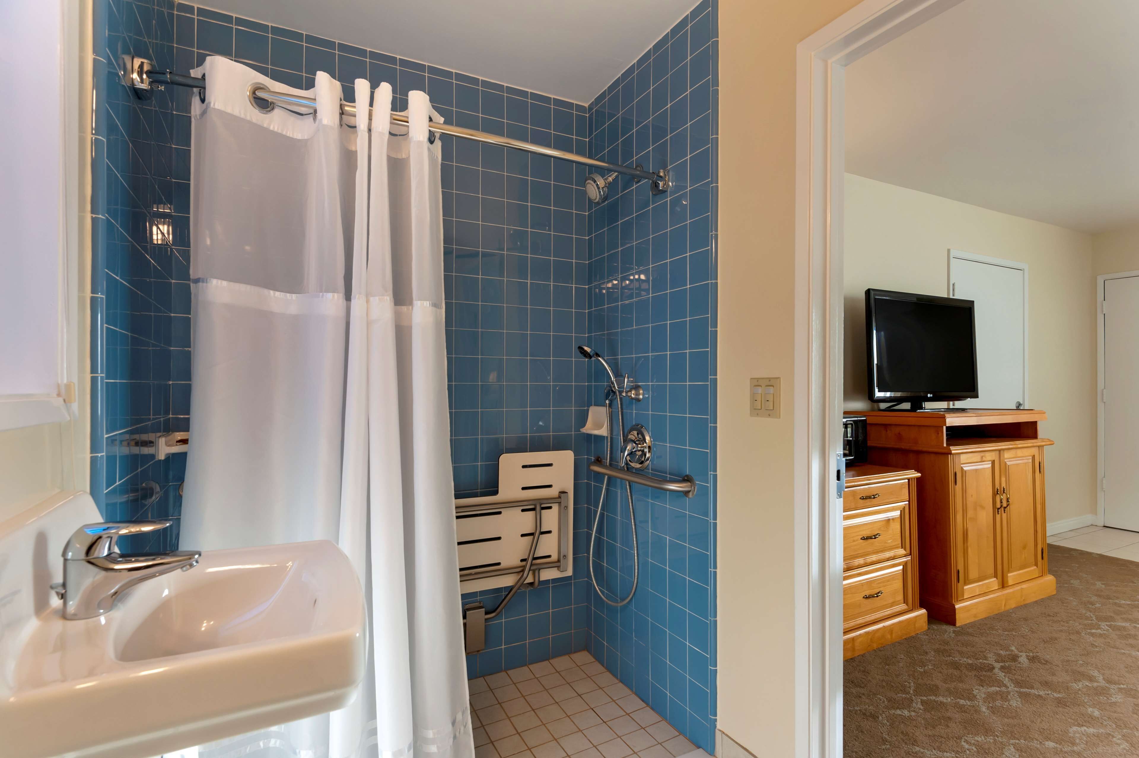 A bathroom with a shower, a sink, and a wooden cabinet with a television.
