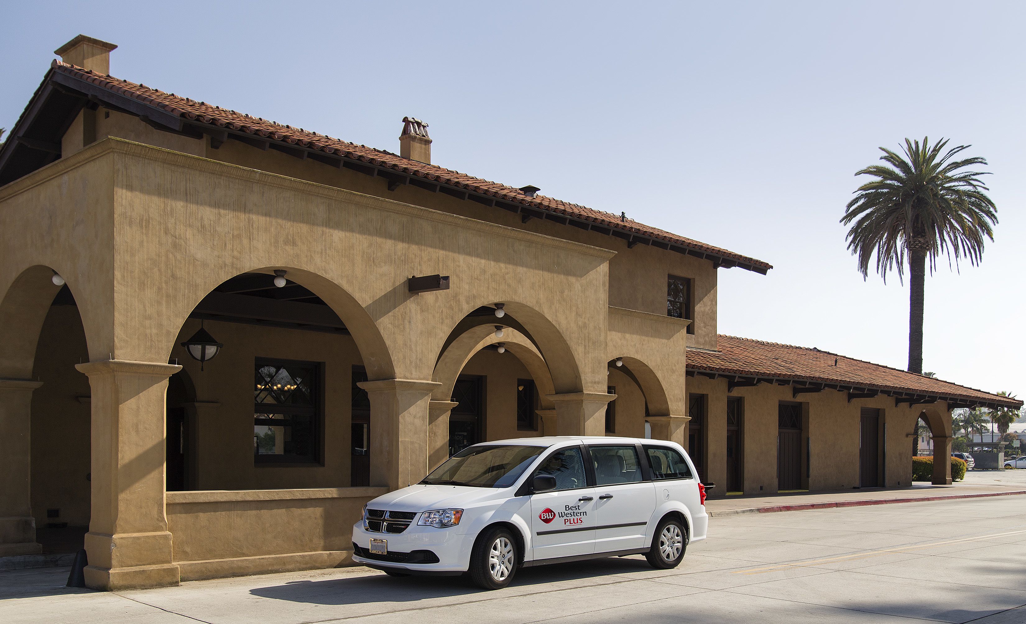 A white van parked in front of a building with a tiled roof and arched windows.