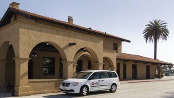 A white van parked in front of a building with a tiled roof and arched windows.