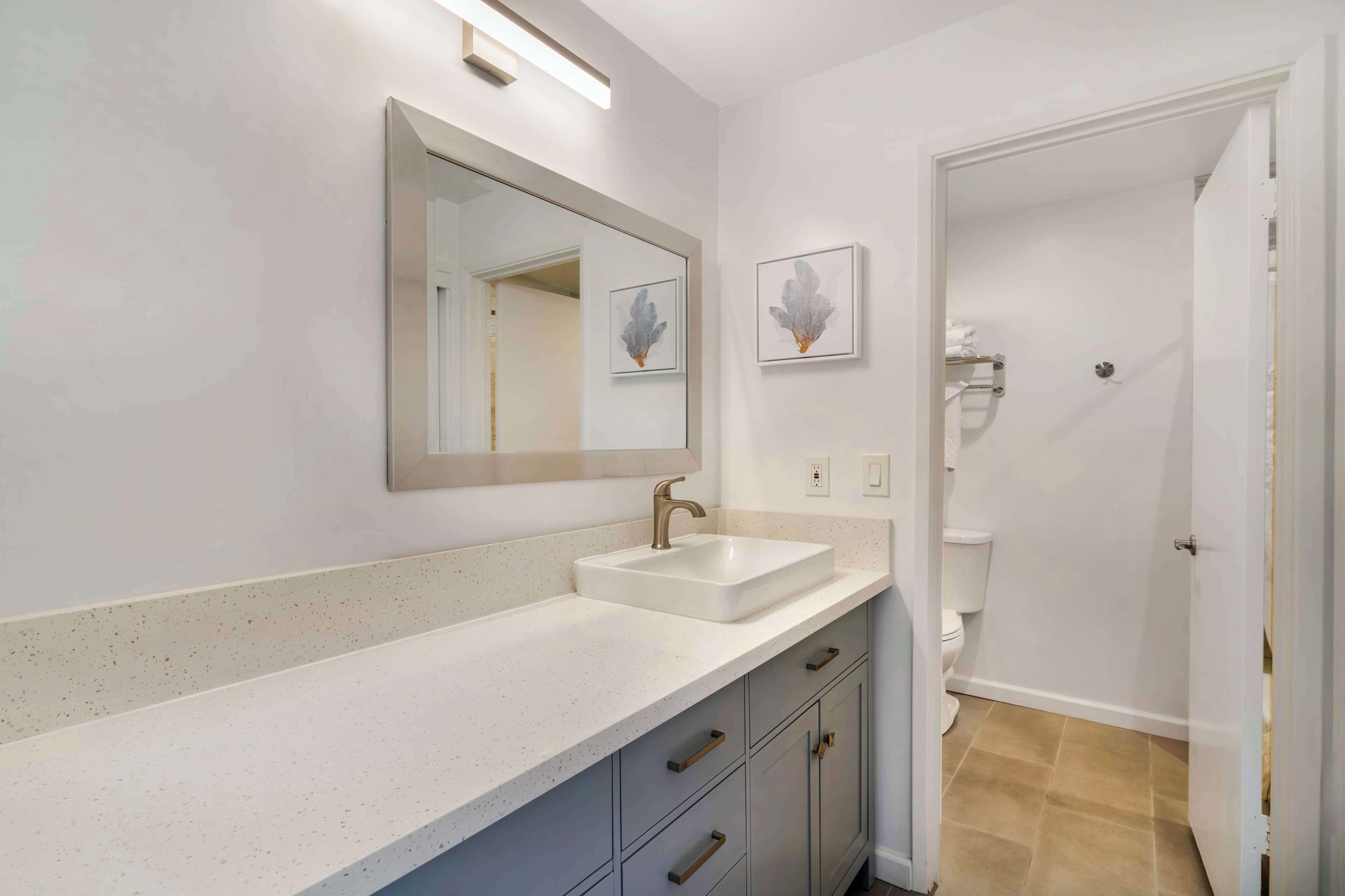 A bathroom with a white sink, a mirror, and two framed artworks on the wall.