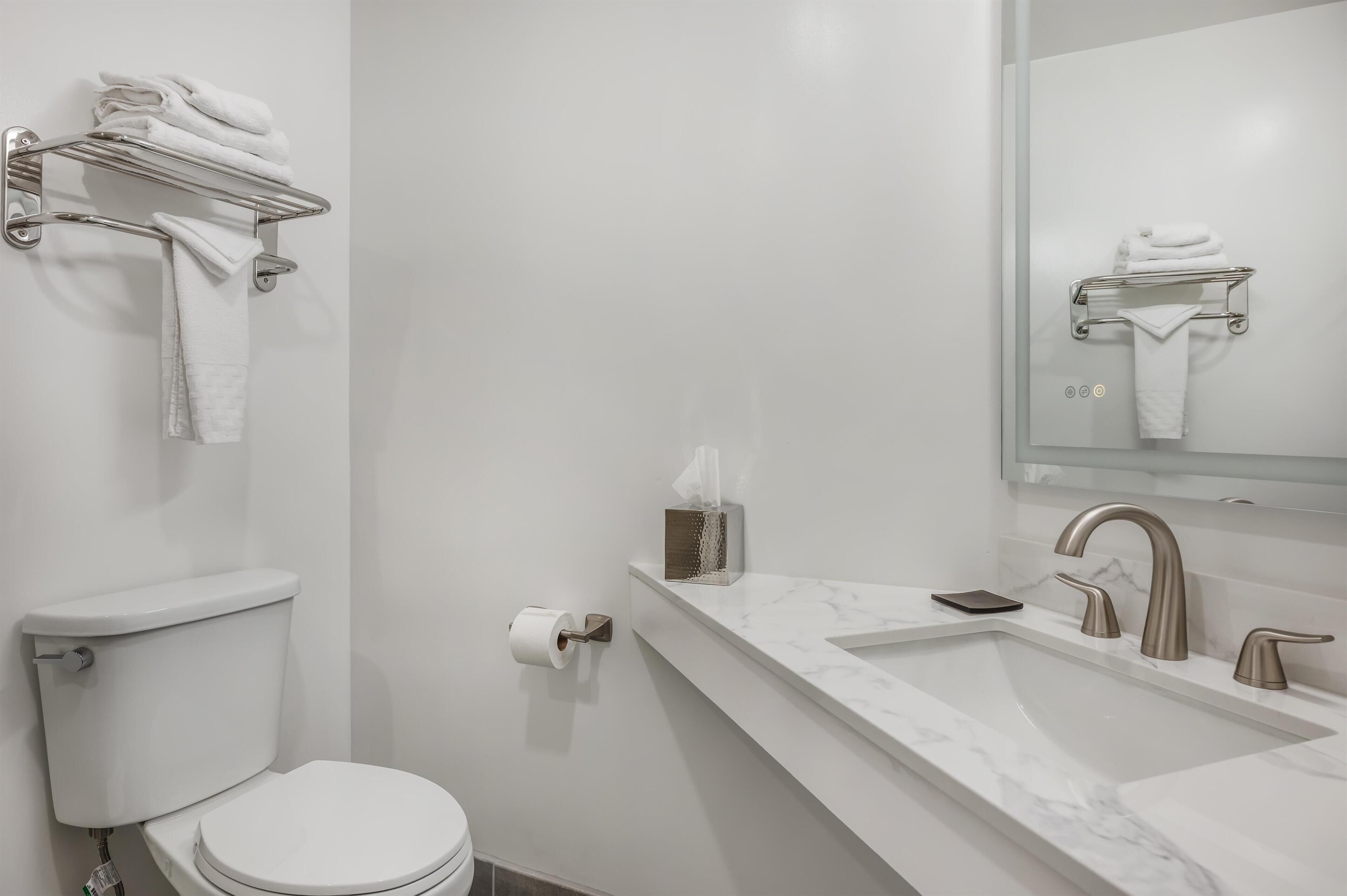 A modern bathroom with a toilet, a towel rack, a sink with a marble countertop, and a mirror.