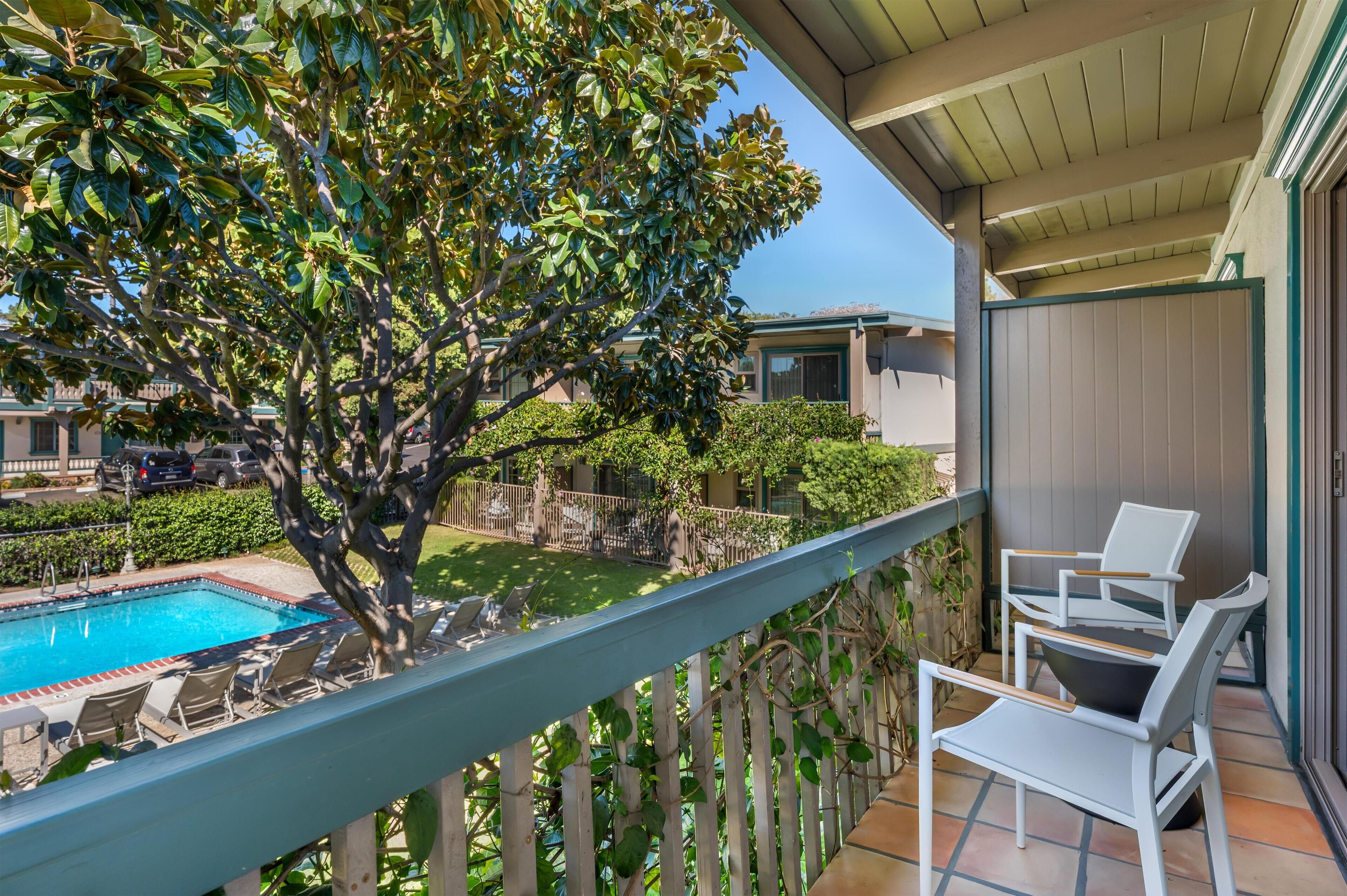 Un balcone con piscina, sedie e un albero.