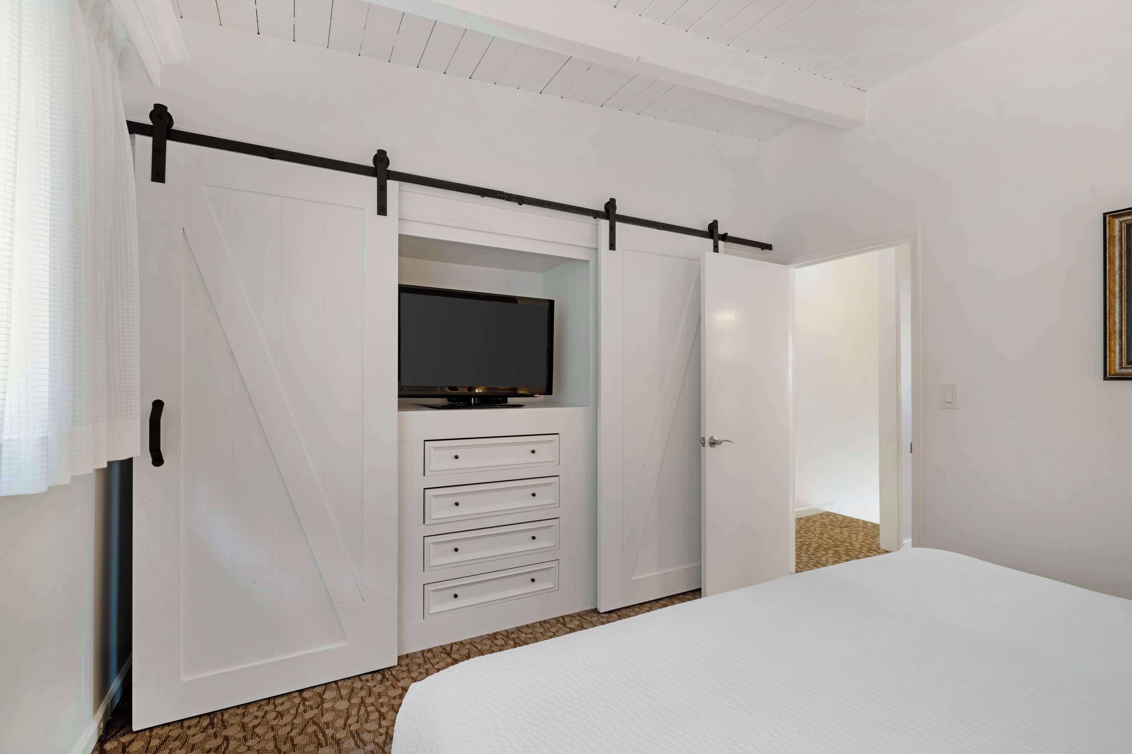 Een slaapkamer met een bed, een schuifdeurkast met een televisie, en een deur naar een andere kamer.