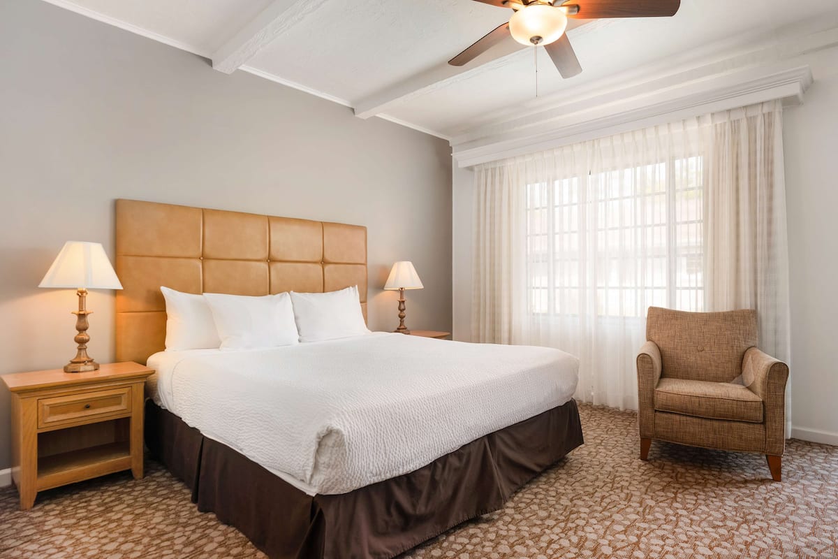 Une chambre d’hôtel avec un grand lit, deux tables de chevet avec des lampes, une chaise et un ventilateur de plafond.
