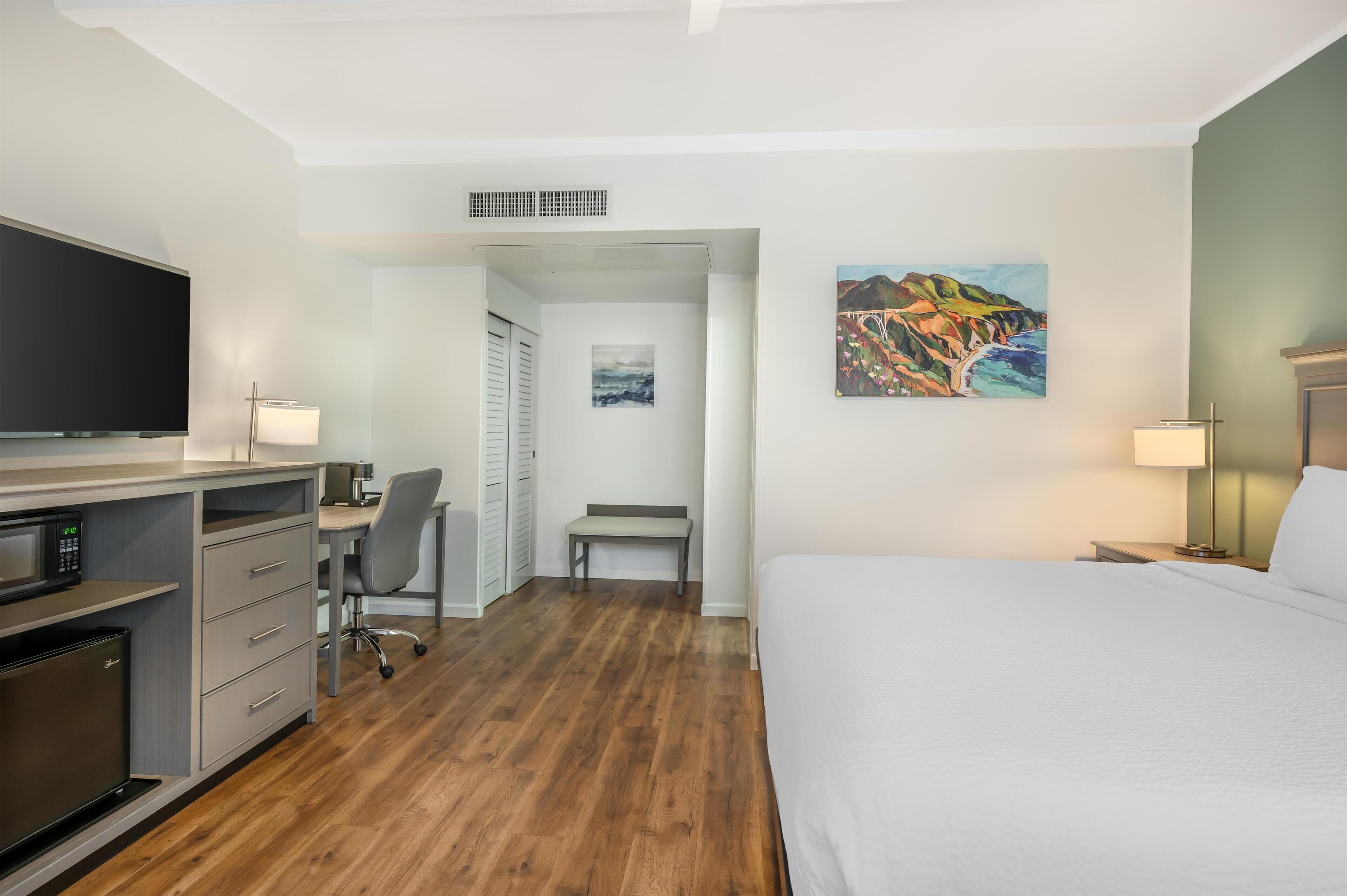 Une chambre d’hôtel avec un lit, un bureau, une chaise et un tableau au mur.