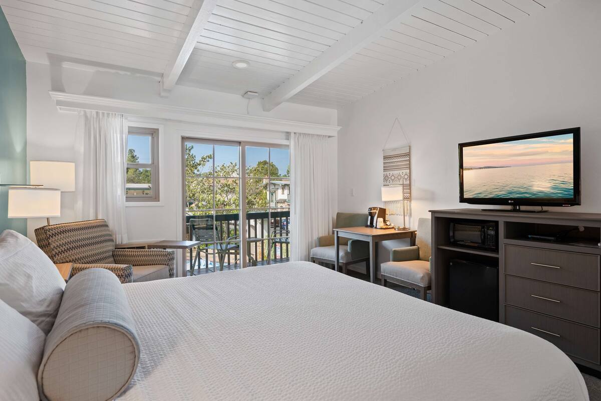 Une chambre d’hôtel dotée d’un grand lit, d’une télévision, d’un bureau avec une chaise et d’un balcon avec des meubles d’extérieur.