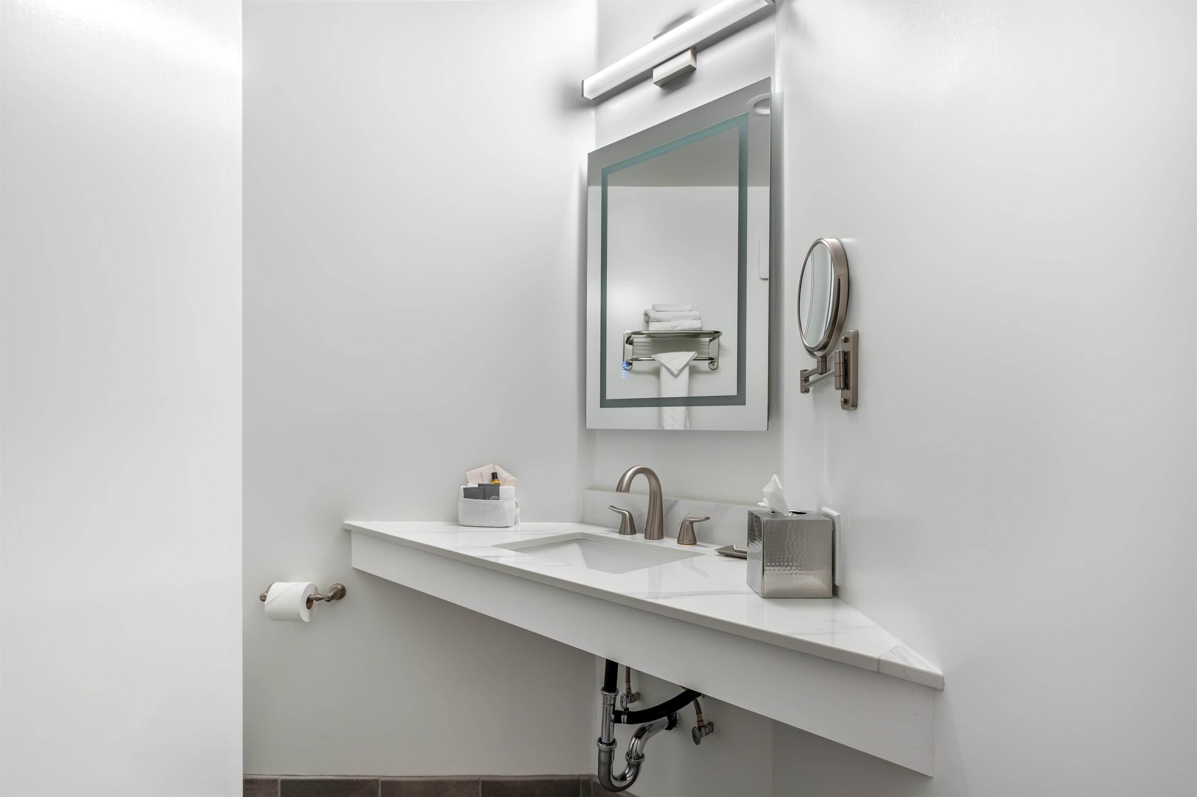 A modern bathroom with a white sink, a mirror, a towel rack, and a toilet paper holder.